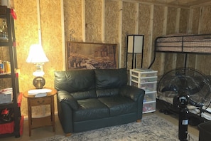 Una habitación con sofá de cuero, lámpara, cuadro, ventilador y unidades de almacenamiento.