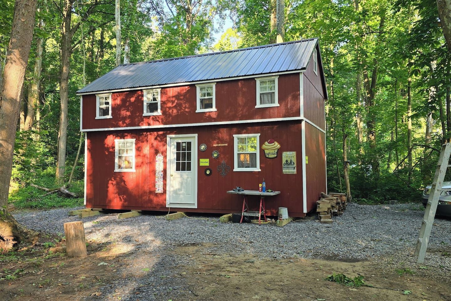 A red two-story building with a gravel driveway, surrounded by trees.