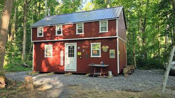 A red two-story building with a gravel driveway, surrounded by trees.