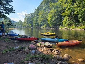 A riverbank with kayaks and a person standing by the water.