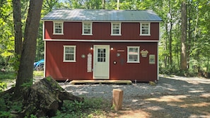 Une cabane en bois rouge, avec une porte blanche, de nombreuses fenêtres et un chemin de gravier menant à l’entrée.