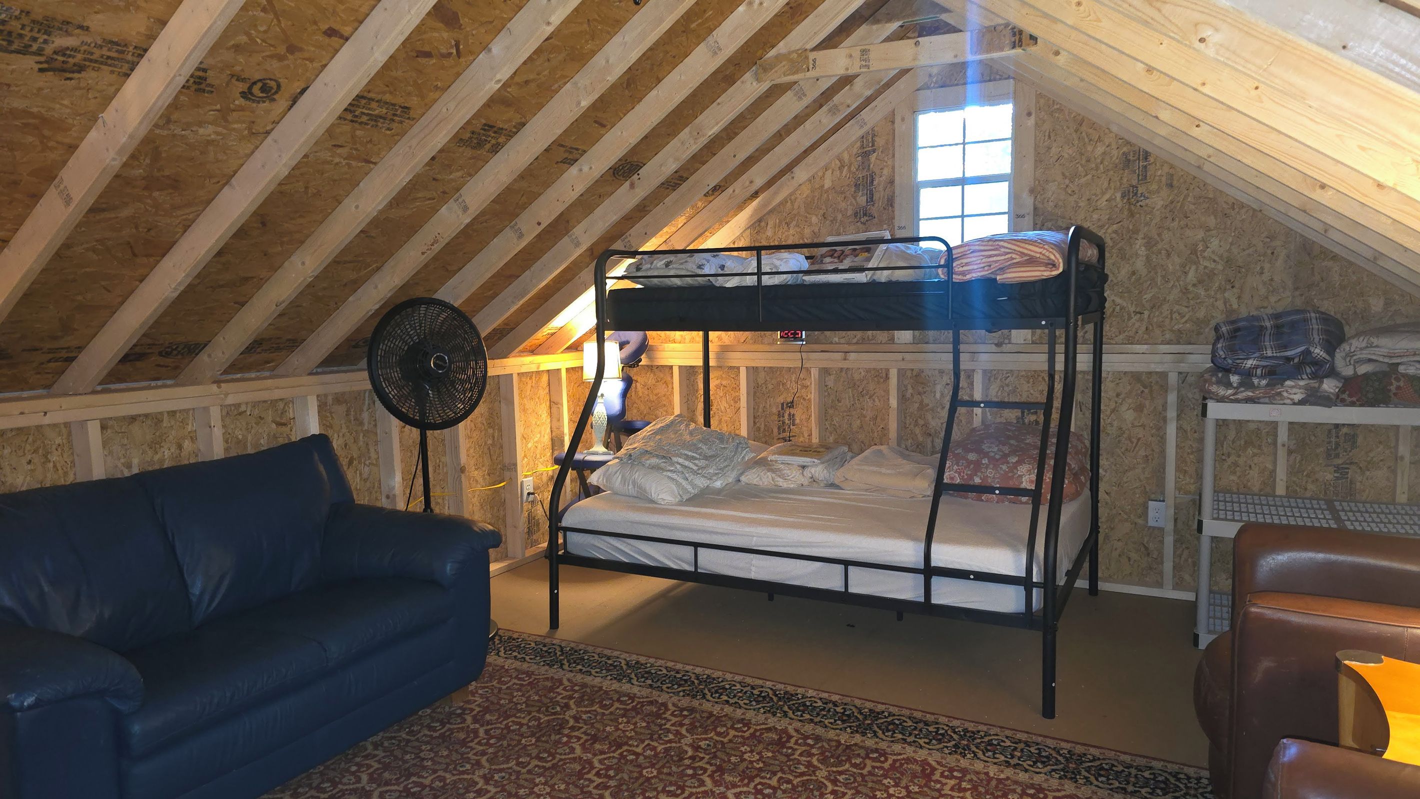 Un lit superposé dans une chambre aménagée en mezzanine, avec un ventilateur, un bureau et un canapé bleu.