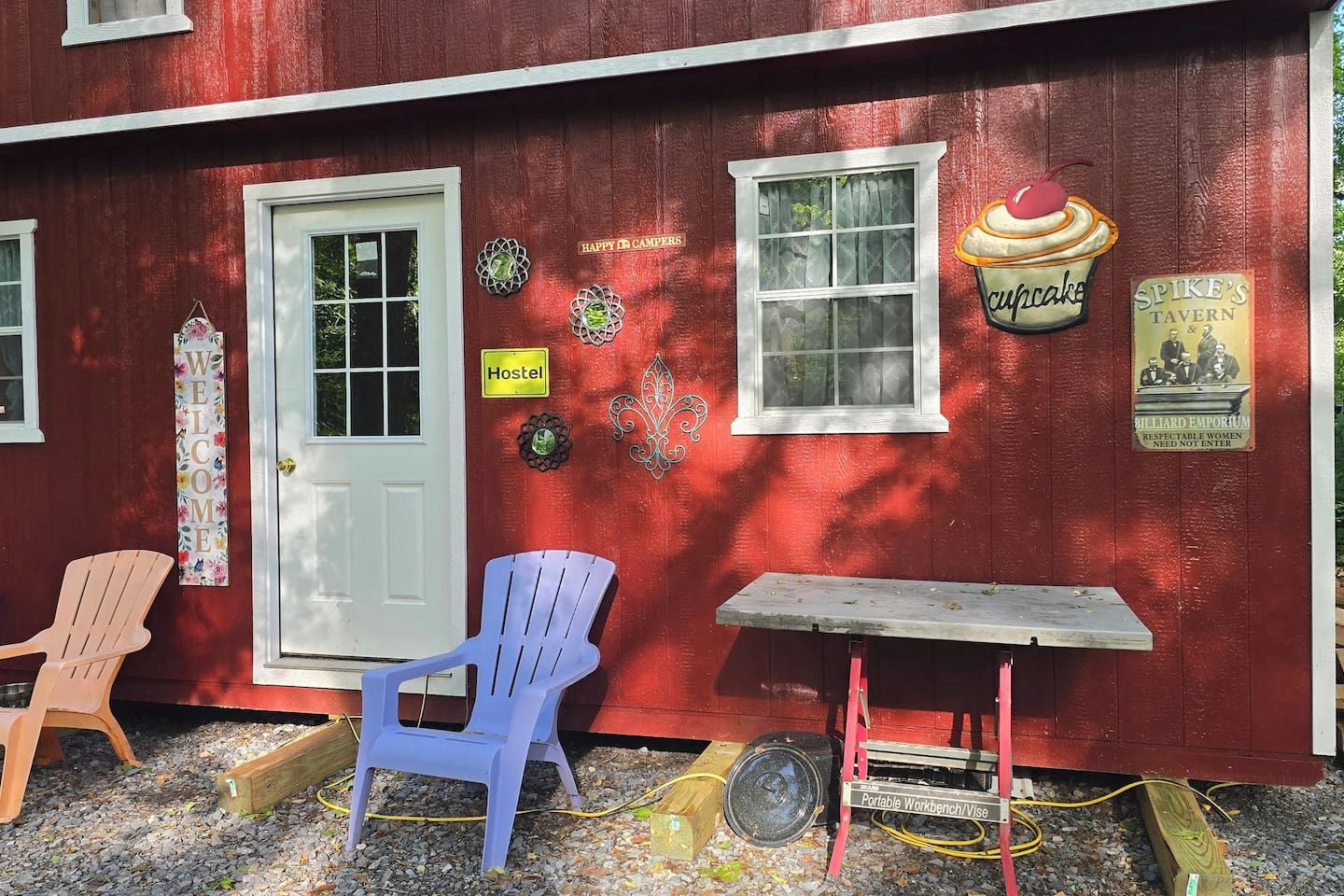 Un edificio rosso con una porta bianca, un cartello con la scritta 'Ostello', uno striscione con 'Benvenuti', un cartello con 'Cupcake' e un cartello per 'Spike's Tavern & Billiard Emporium'.