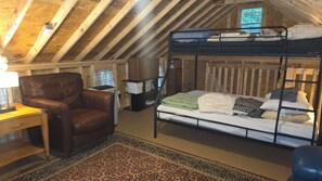 Un dormitorio acogedor en el desván con una cama litera, un sillón de cuero, un escritorio y una alfombra estampada.