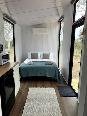 Un dormitorio con cama, almohadas, una mesita de noche con microondas y vistas al exterior.