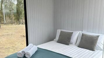 Een slaapkamer met een bed, kussens, een laptop en een raam.