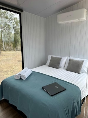 Un dormitorio con cama, almohadas, una computadora portátil y una ventana.