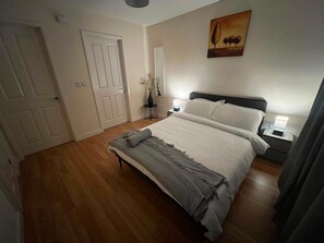 A bedroom with a bed, bedside tables, a nightstand, a door, and a wall-mounted painting.