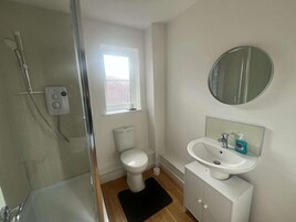 Un baño con cabina de ducha de vidrio, inodoro, lavabo con espejo y ventana.