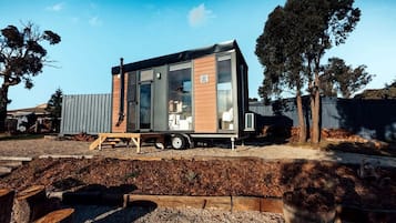 Una casa móvil moderna con techo plano, ventanas amplias y un pequeño remolque adosado.