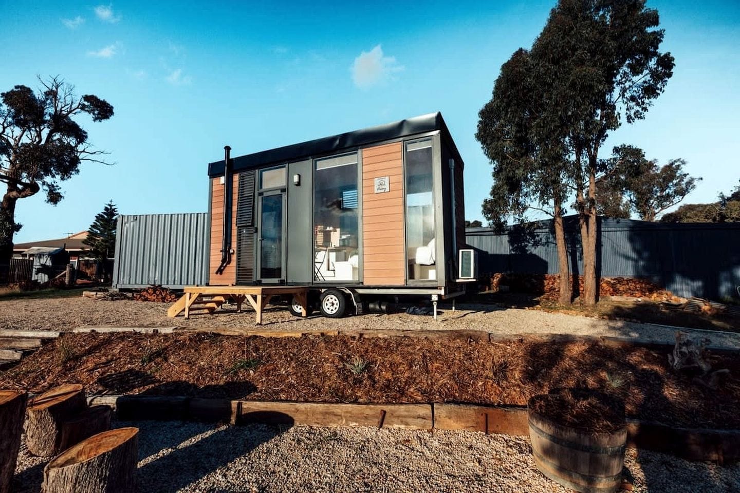 Una casa móvil moderna con techo plano, ventanas amplias y un pequeño remolque adosado.
