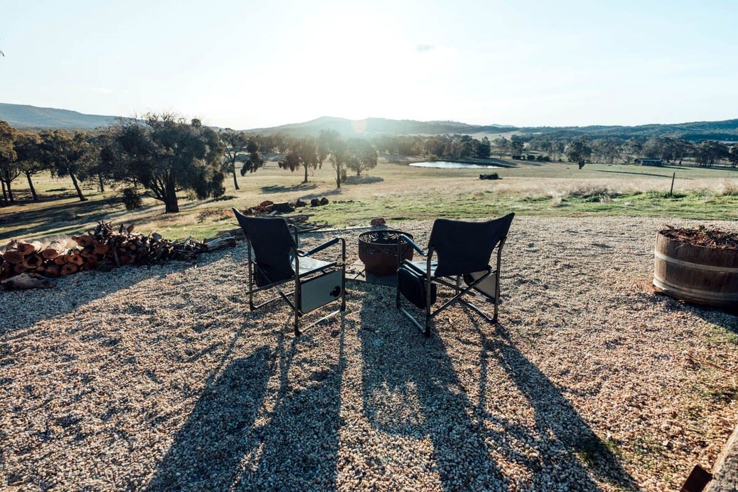 Een terras met twee stoelen en een tafel, omgeven door grind, bomen en een verre weidsheid van heuvels.
