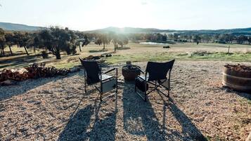 Een terras met twee stoelen en een tafel, omgeven door grind, bomen en een verre weidsheid van heuvels.
