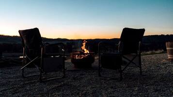 Two chairs facing a campfire with a view of a sunset over a hilly landscape.