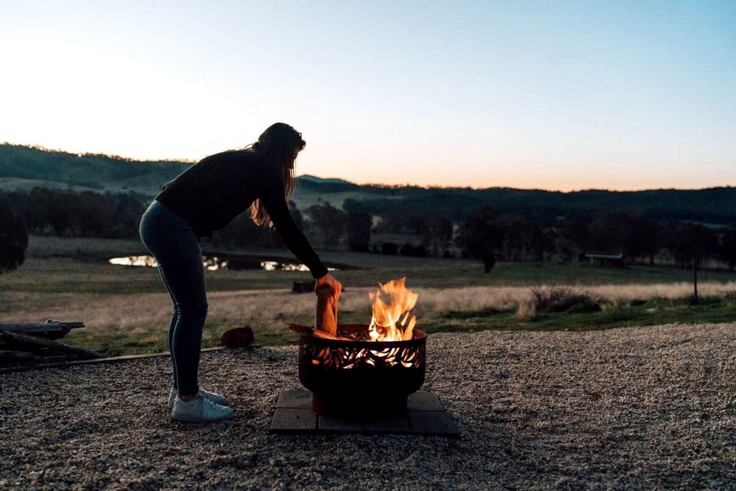 A person tending to a fire in a metal fire pit outdoors.