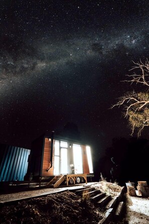 A small cabin with a window, a wooden deck, and a starry night sky.