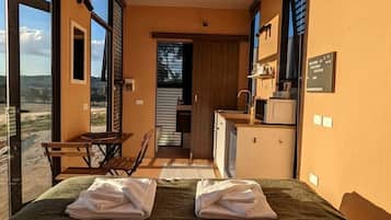 Una habitación con cama, una mesita, una silla, kitchenette y vistas al exterior.