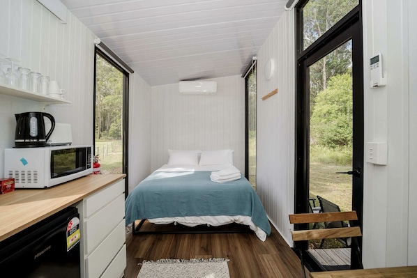 Quarto compacto com cama, micro-ondas e uma pequena mesa com chaleira.