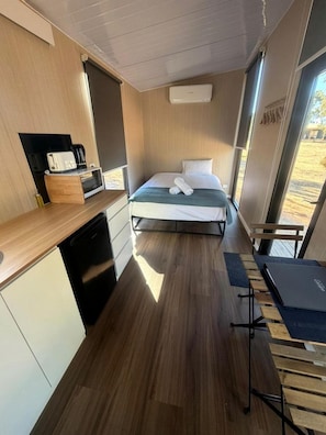 A compact room with a bed, a small kitchenette, and a window.