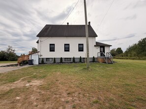 A single-story white house with a dark roof, a front porch, and a small deck.
