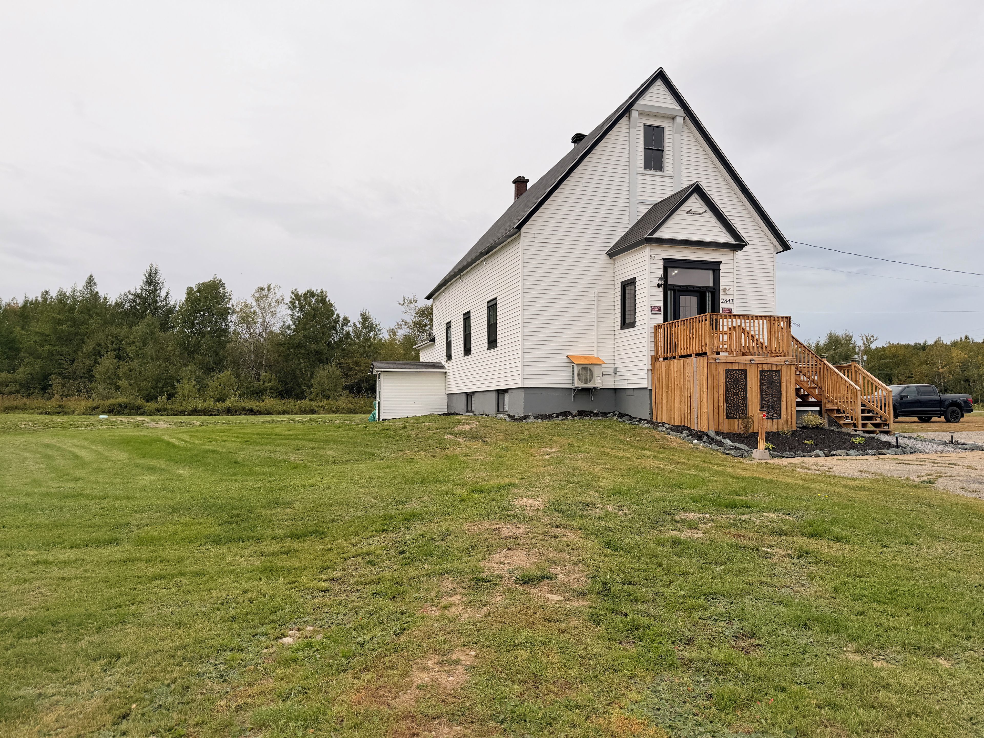 Une maison blanche à deux étages, dotée d’une terrasse en bois et devant laquelle est garé un camion noir.