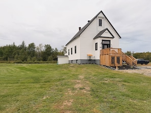 A white two-story house with a wooden deck and a black truck parked in front.