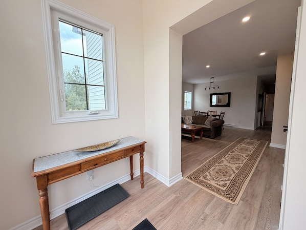 A hallway with a wooden bench, a patterned rug, and a dining area with a table and chairs.