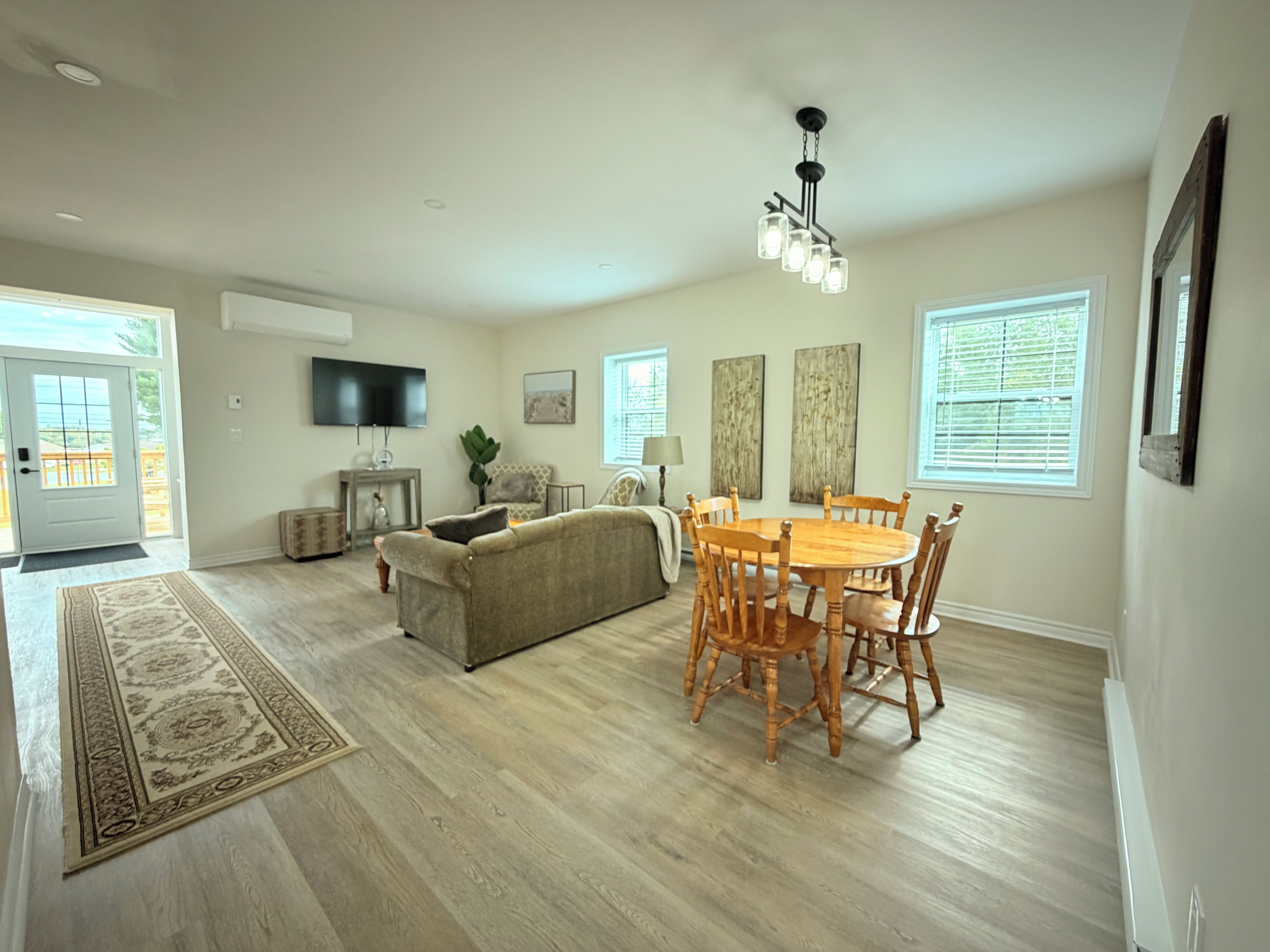 A spacious living room with a sofa, dining table, and chairs, a flat-screen TV, and a large window with blinds.