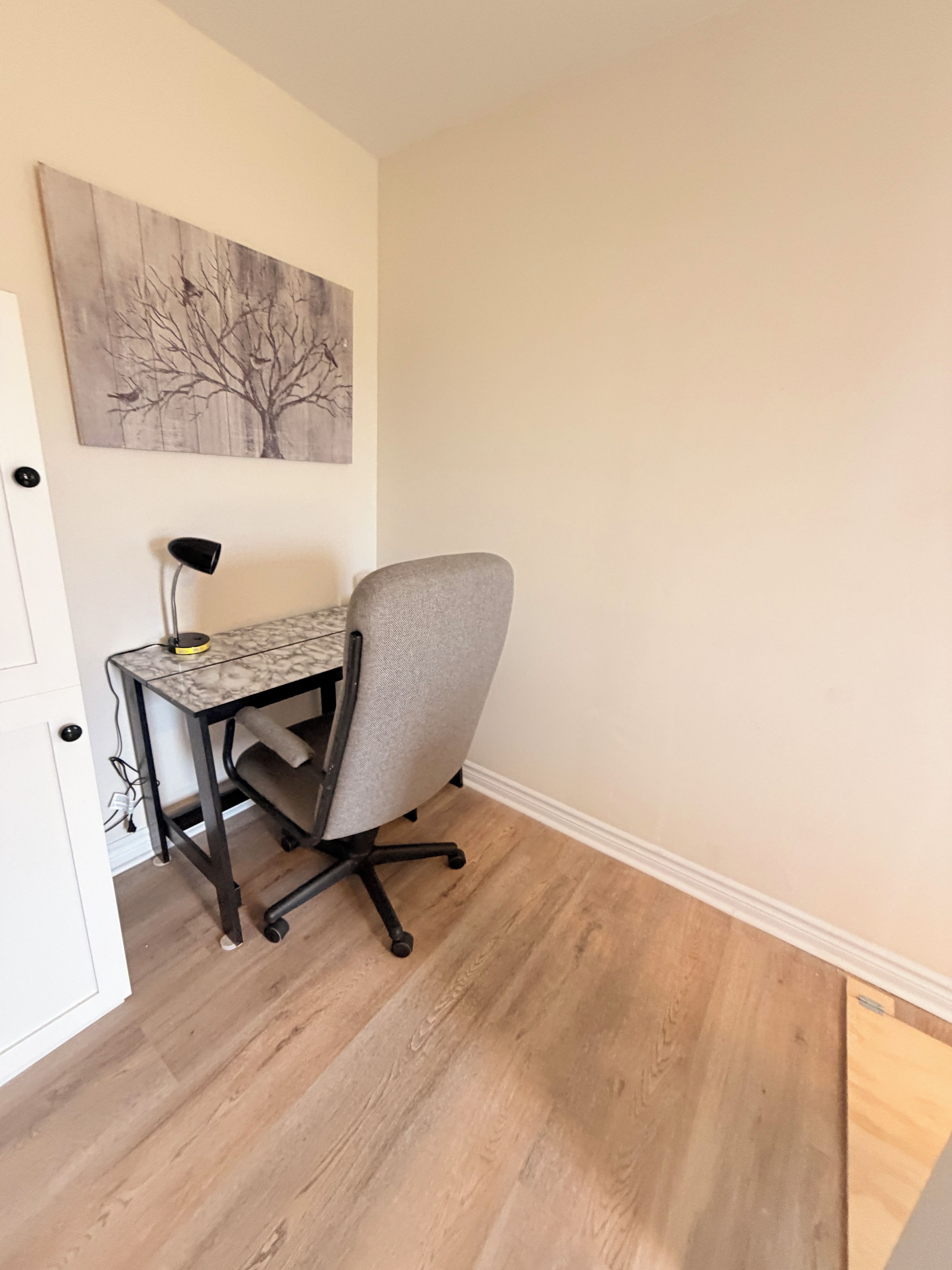 Une pièce avec un bureau, une chaise et un tableau au mur.