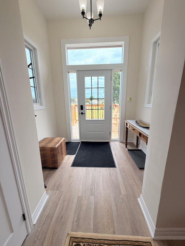 A hallway with a wooden floor, a white door with a view to the outside, and a bench with a tray.