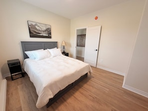 A bedroom with a bed, nightstands, a lamp, a door, and a wall-mounted picture.
