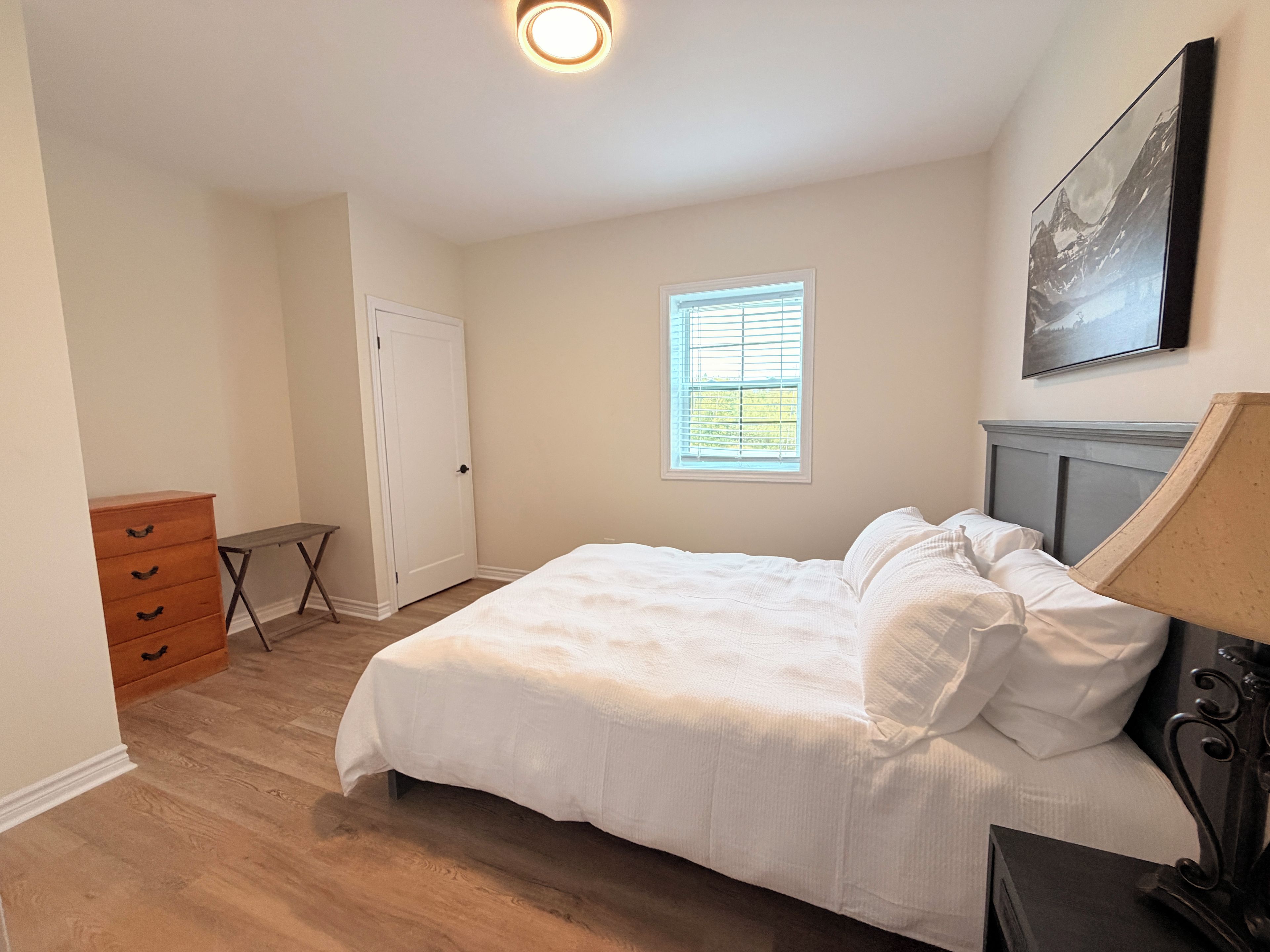 Ein Schlafzimmer mit Bett, Kommode, Fenster und einem Bild an der Wand.