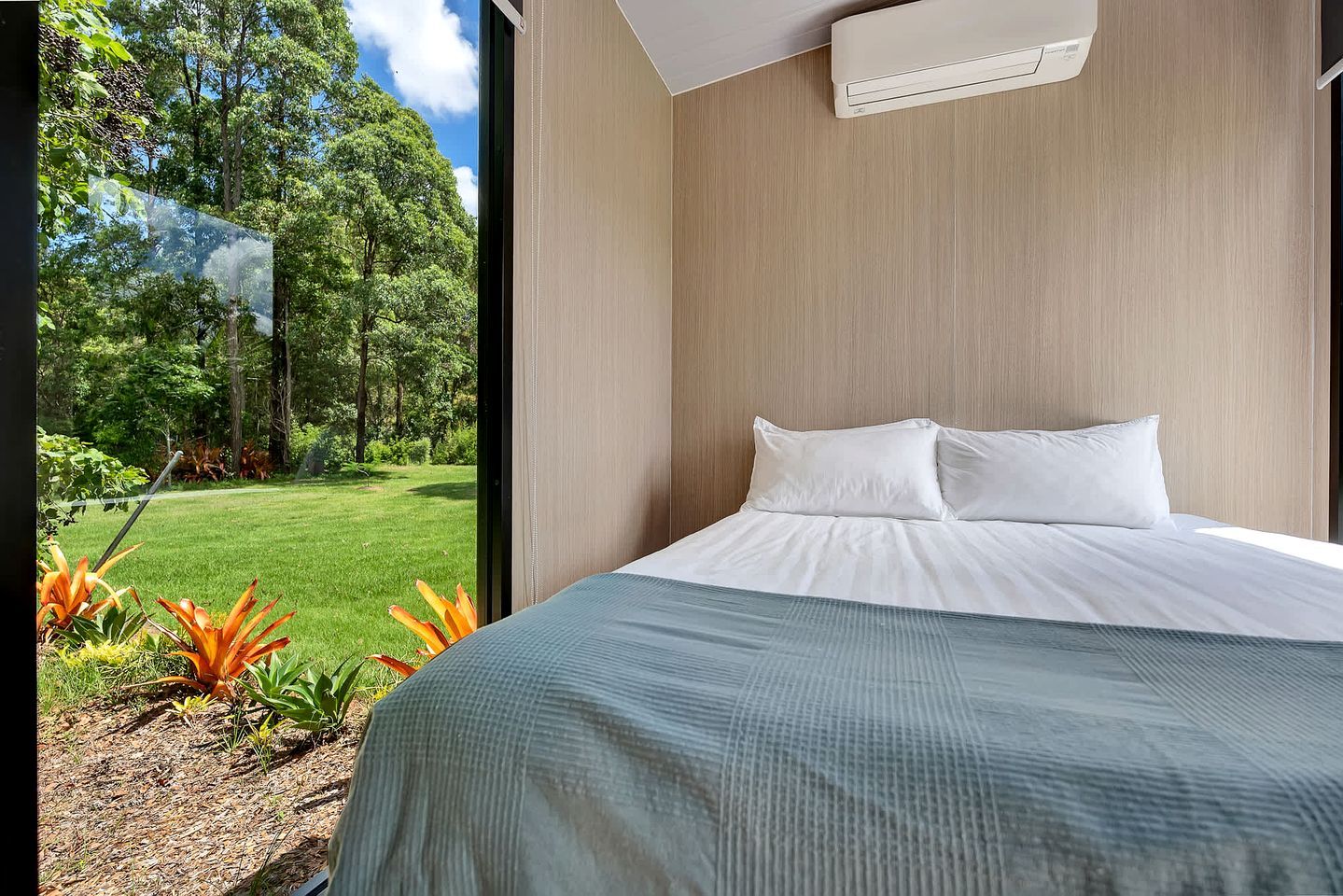 A bedroom with a large bed, a window, and a view of a garden.