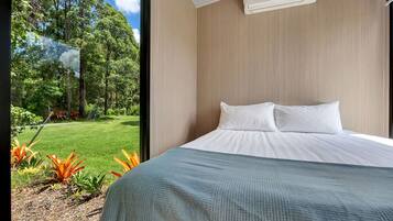 A bedroom with a large bed, a window, and a view of a garden.