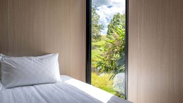 Un dormitorio con un ventanal grande, una cama con ropa blanca y vistas a zonas verdes.