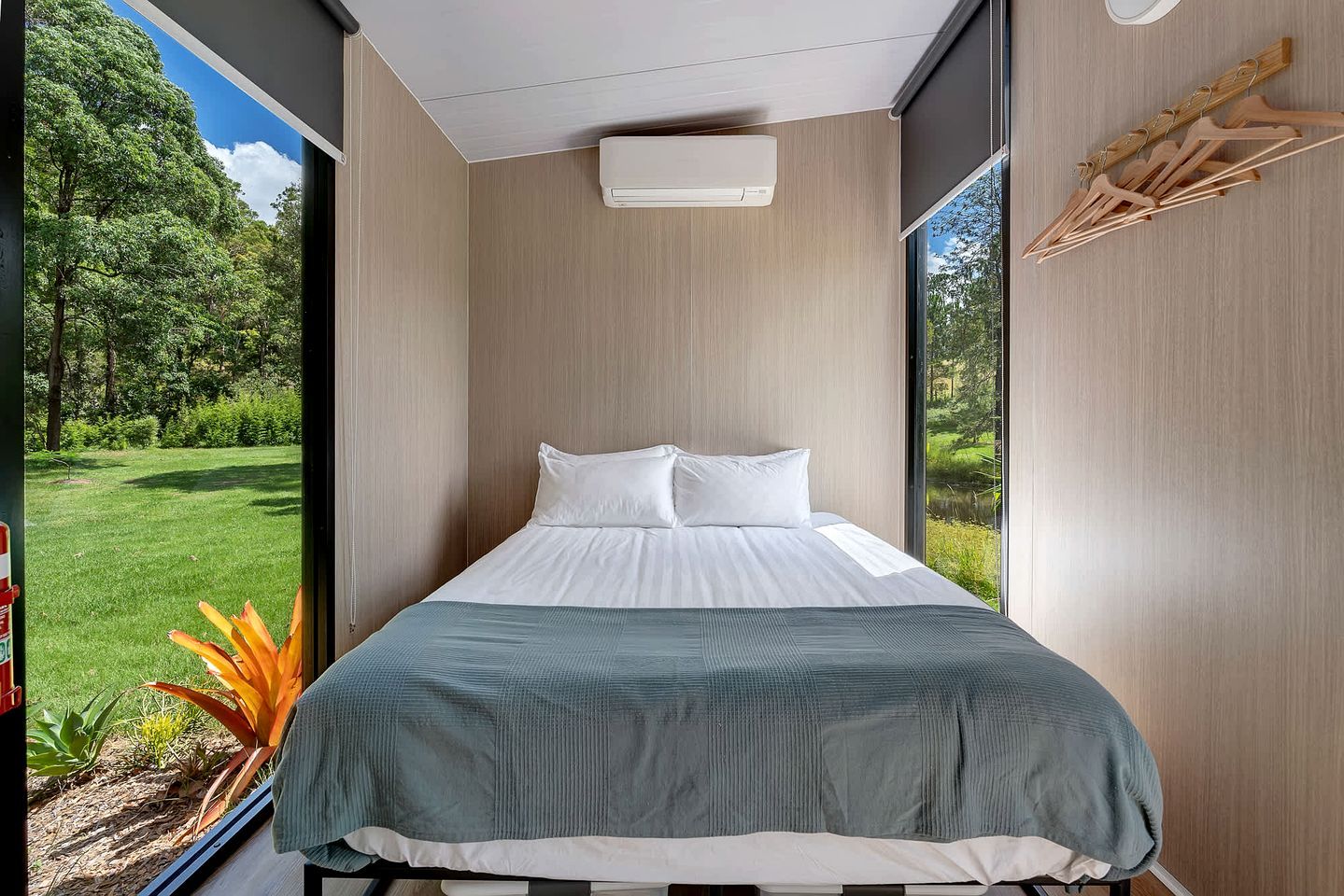 A modern bedroom with a large window, a bed with white linens, and a view of a green landscape.