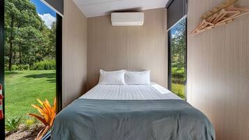 A modern bedroom with a large window, a bed with white linens, and a view of a green landscape.