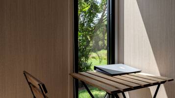 A wooden table with a laptop, a chair, and a view of greenery through a window.