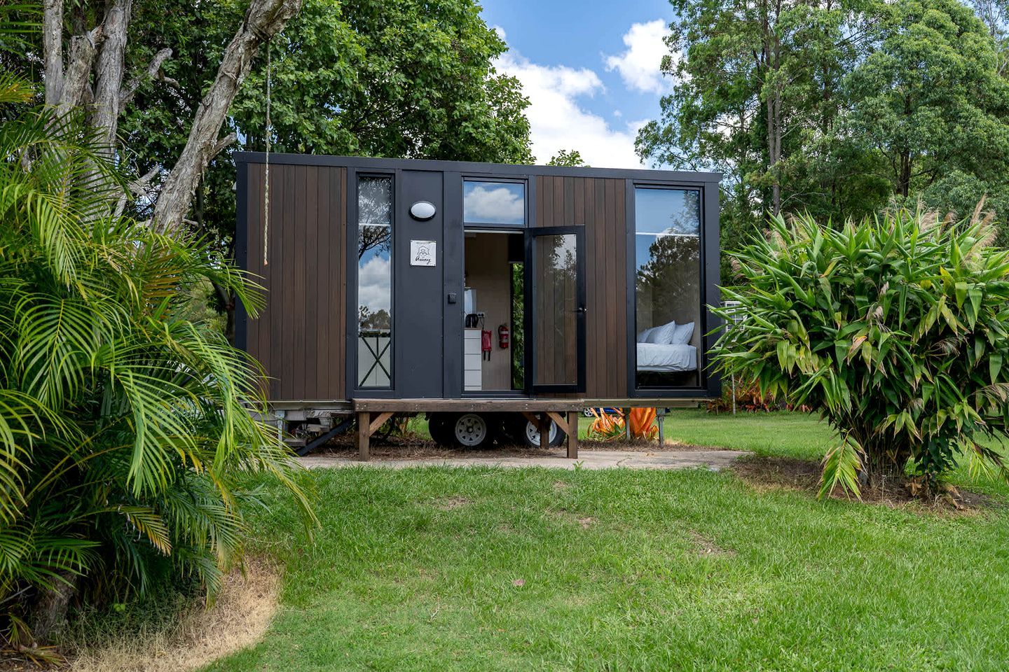 A modern, compact mobile home with a sleeping area and kitchenette, situated in a lush garden.