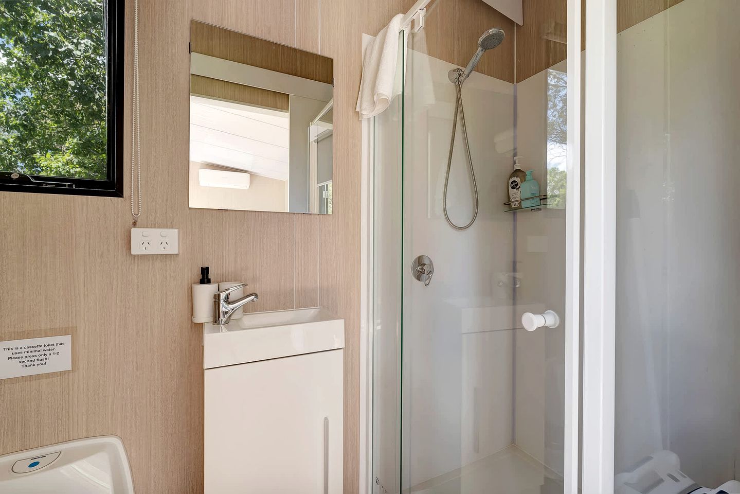 A modern bathroom with a glass shower enclosure, a sink with a mirror, and a towel hanging on the door.