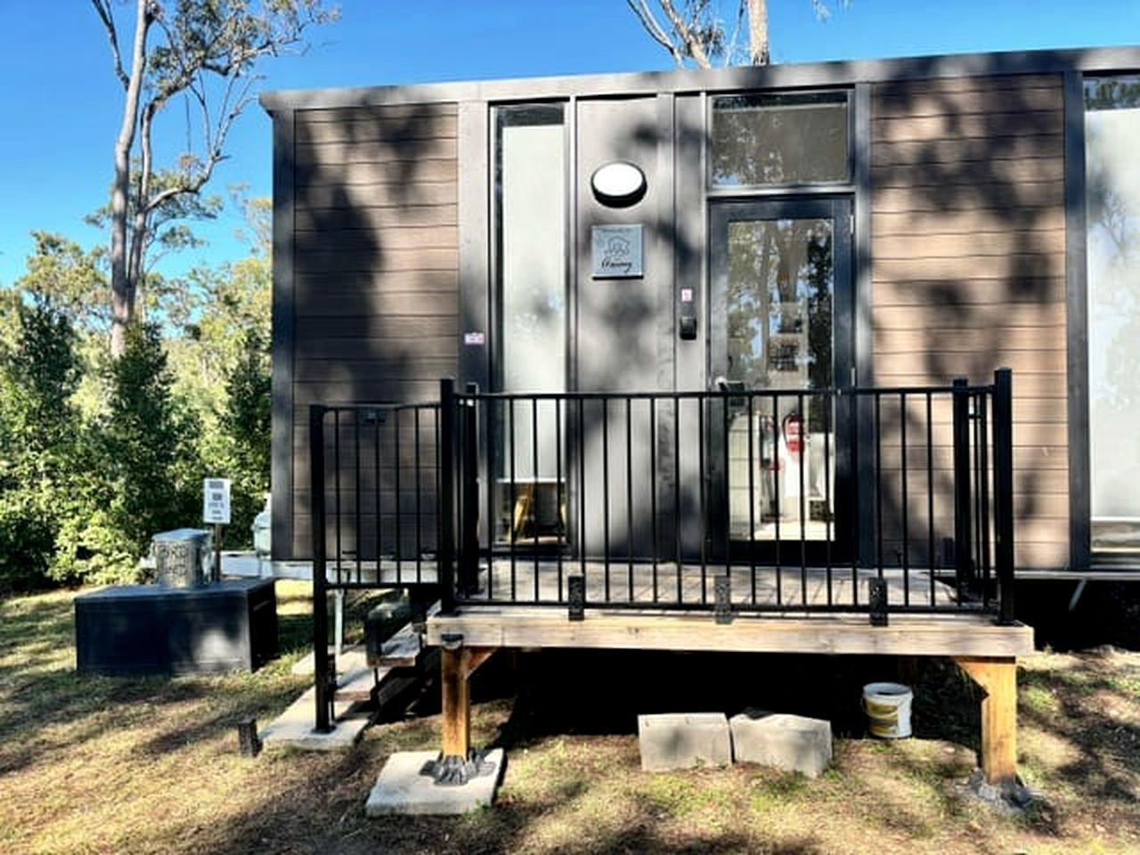 A small, single-story cabin with a front porch and a metal railing.