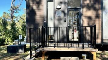 A small, single-story cabin with a front porch and a metal railing.