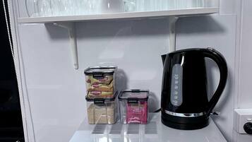 Eine Mikrowelle zusammen mit einer Kaffeemaschine, einem Baukasten an Gläsern und Gewürzbehältern auf einer Ablagefläche.