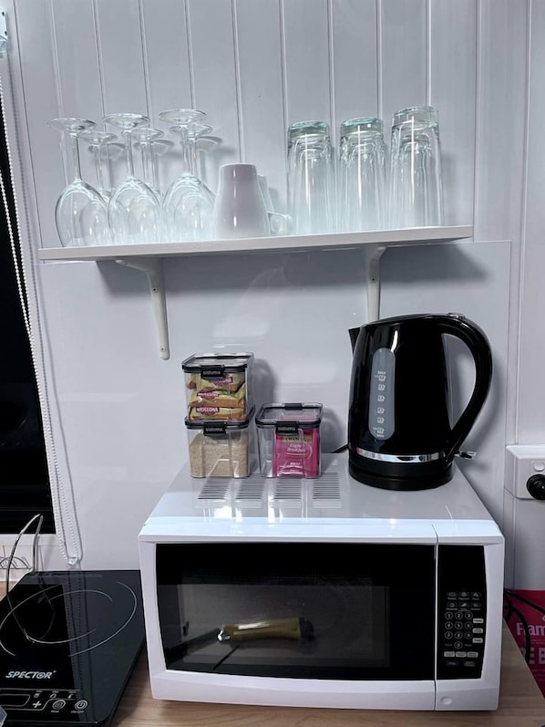 A microwave oven with a coffee maker, a set of glassware, and condiment containers on a shelf.