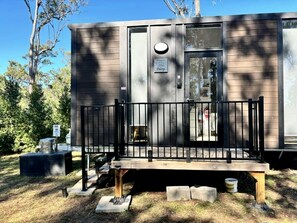 A small, single-story cabin with a front porch and a metal railing.