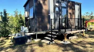 A modern, two-story cabin with a balcony, surrounded by trees and a clear sky.
