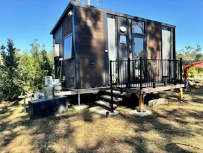 Une cabane moderne à deux étages, dotée d’un balcon, entourée d’arbres et offrant une vue sur un ciel dégagé.