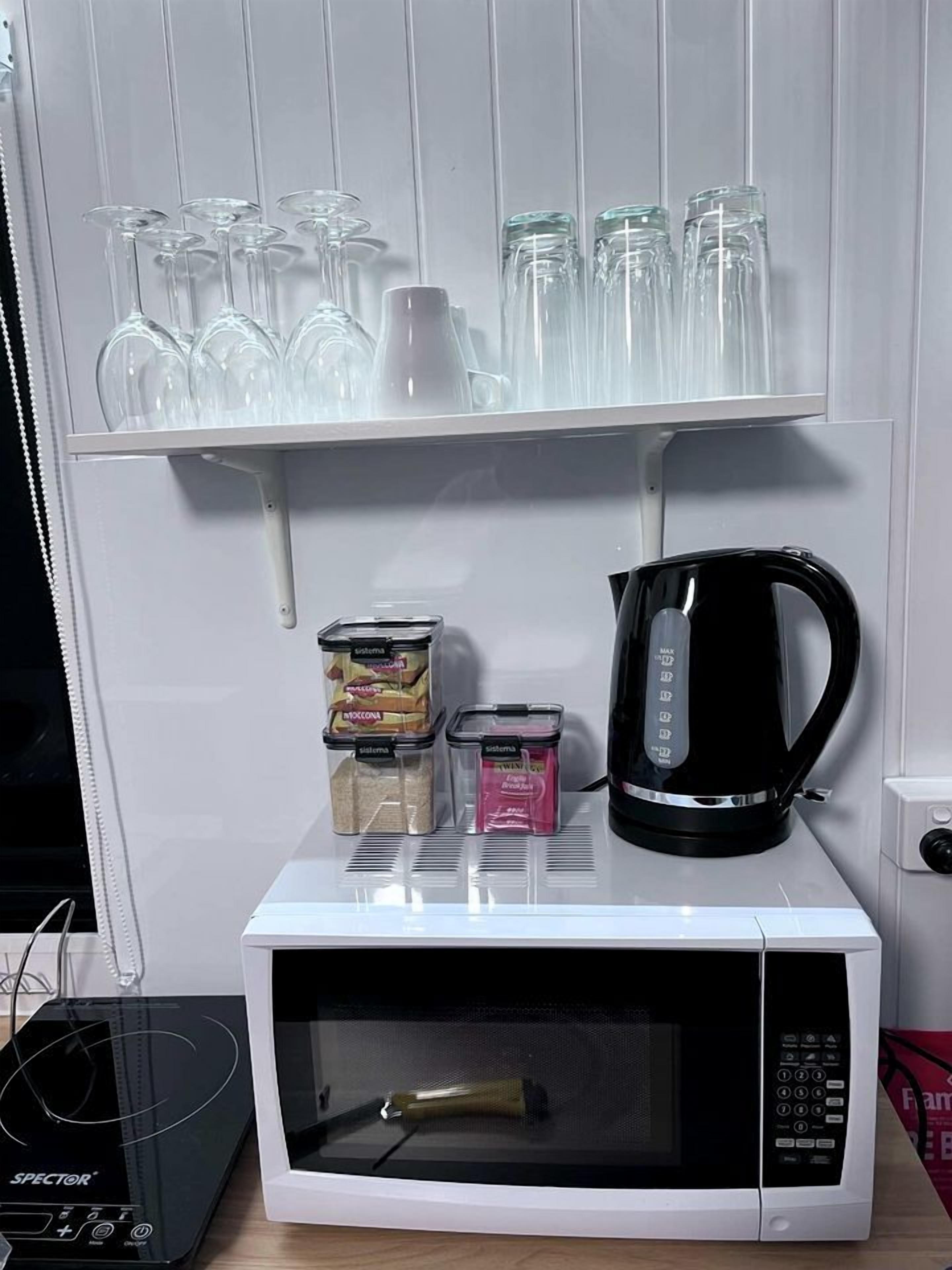 Un four à micro-ondes avec une machine à café, un ensemble de verrerie et des récipients pour les condiments, le tout placé sur une étagère.