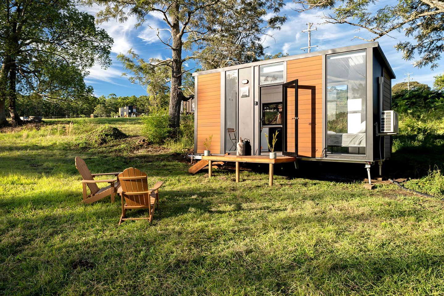Une cabane moderne de plain-pied, dotée d’une porte-fenêtre coulissante, d’une petite terrasse et d’une chaise.