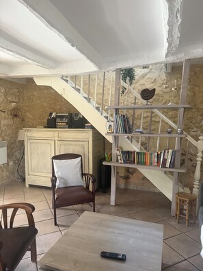 A room with a staircase, a bookshelf, a chair, a table, and a remote control.